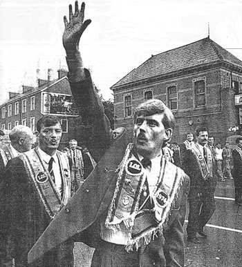 Orangeman holding five fingers aloft outside Graham's bookmakers Ormeau Road 1992 - in celebration of the five nationalists slaughtered there by unionist paramilitaries (while all whistle a sectarian tune)