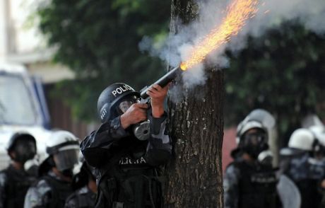 third world cop wearing Kevlar body armour firing tear gas canister at civilians outside the Brazilian embassy to Honduras